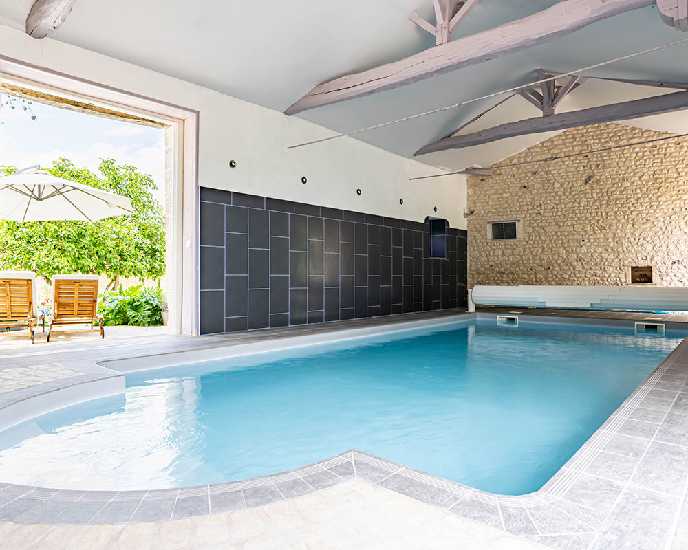 Large blue swimming pool inside limestone building overlooking the garden