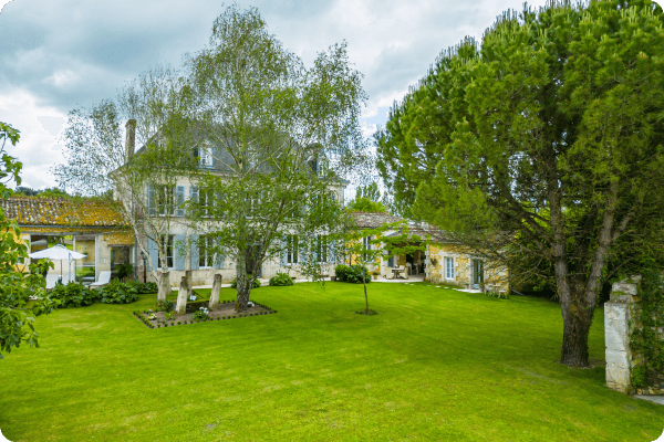 Large open lawn in front of large french house surrounded by large trees